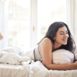 happy young woman browsing phone on bed